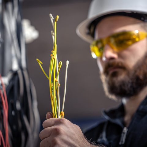Male electrician at the checkout counter on a blurred background of a switchboard.