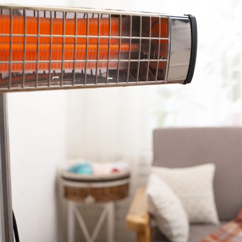 Electric infrared heater warming up living room with sofa and potted plant at background